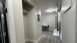 A hallway with a wooden floor, a dining area with chairs and a table, and a TV on a stand. - Deluxe One-Bedroom Apartment with City View (Oshawa)