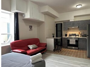 A compact living space with a red sofa, a small kitchen area, and a bed.