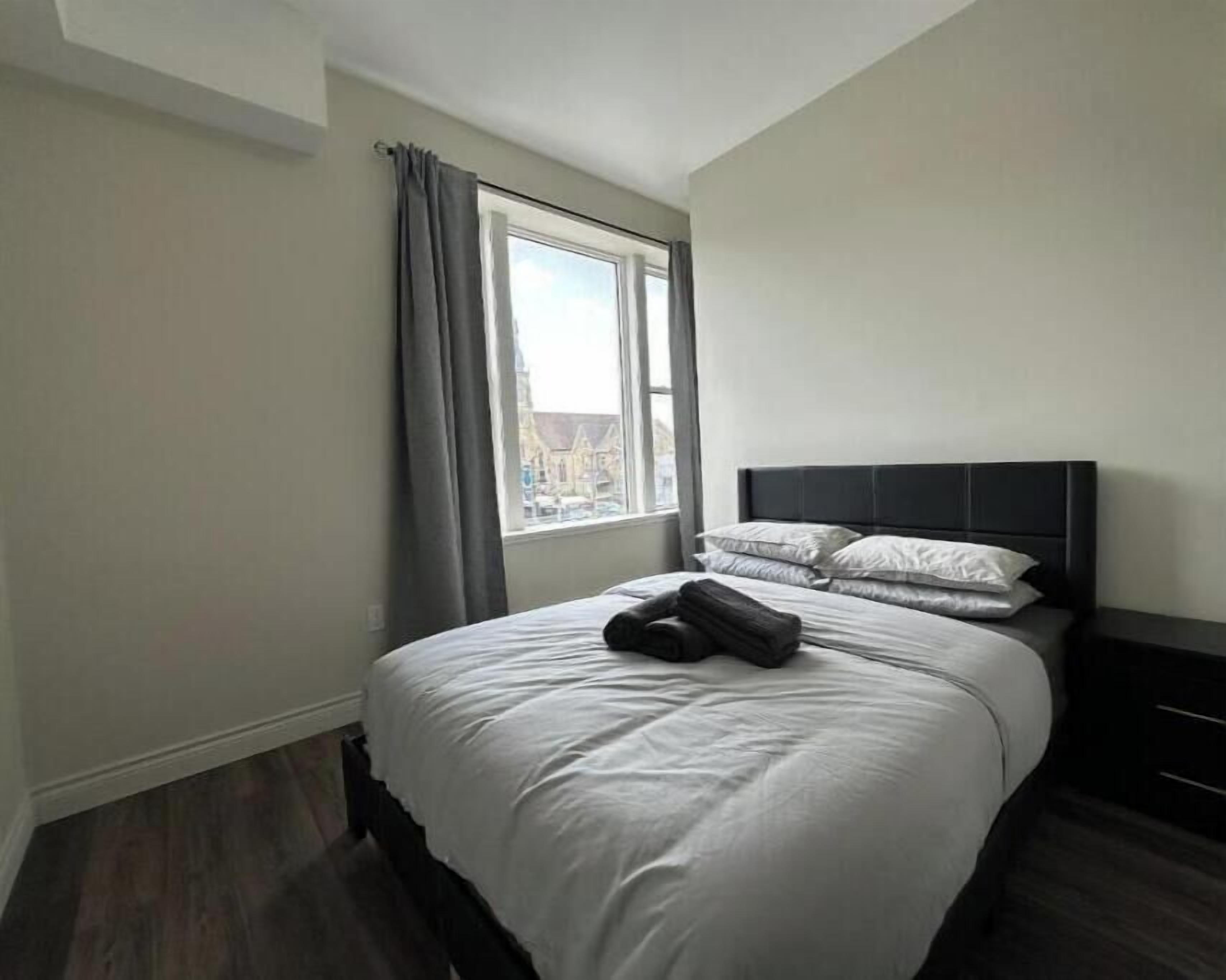 Una habitación de hotel con una cama grande, una ventana con cortinas y vistas a edificios.