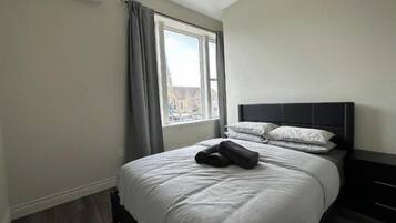 Una habitación de hotel con una cama grande, una ventana con cortinas y vistas a edificios.