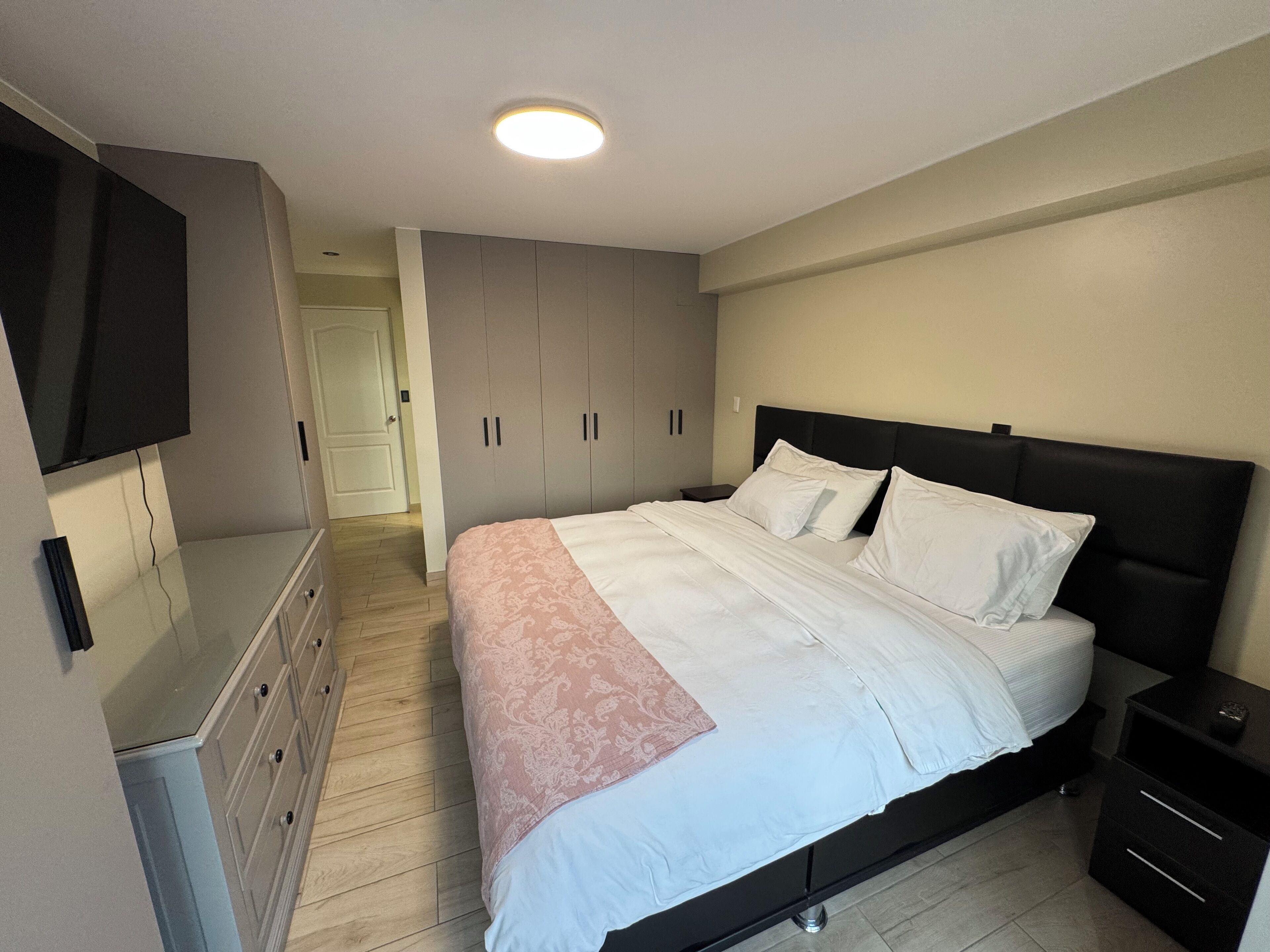 A bedroom with a bed, a dresser, a TV, and a wardrobe.