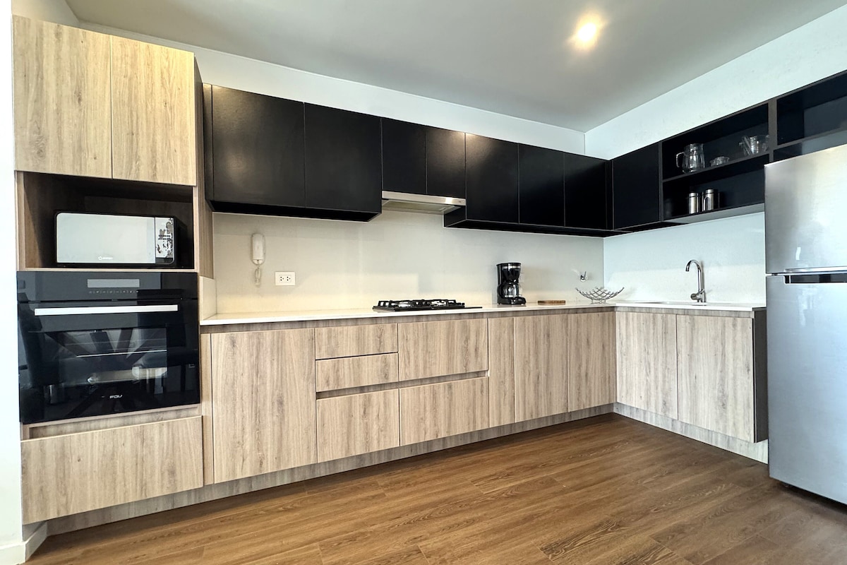 Una cocina moderna con armarios de madera, horno integrado, cafetera y refrigerador de acero inoxidable.