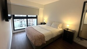 A bedroom with a bed, bedside tables, a window, and a flat-screen TV mounted on the wall. - Aparts4Days 1 Bedroom Apartment Miraflores 4255 (Lima)