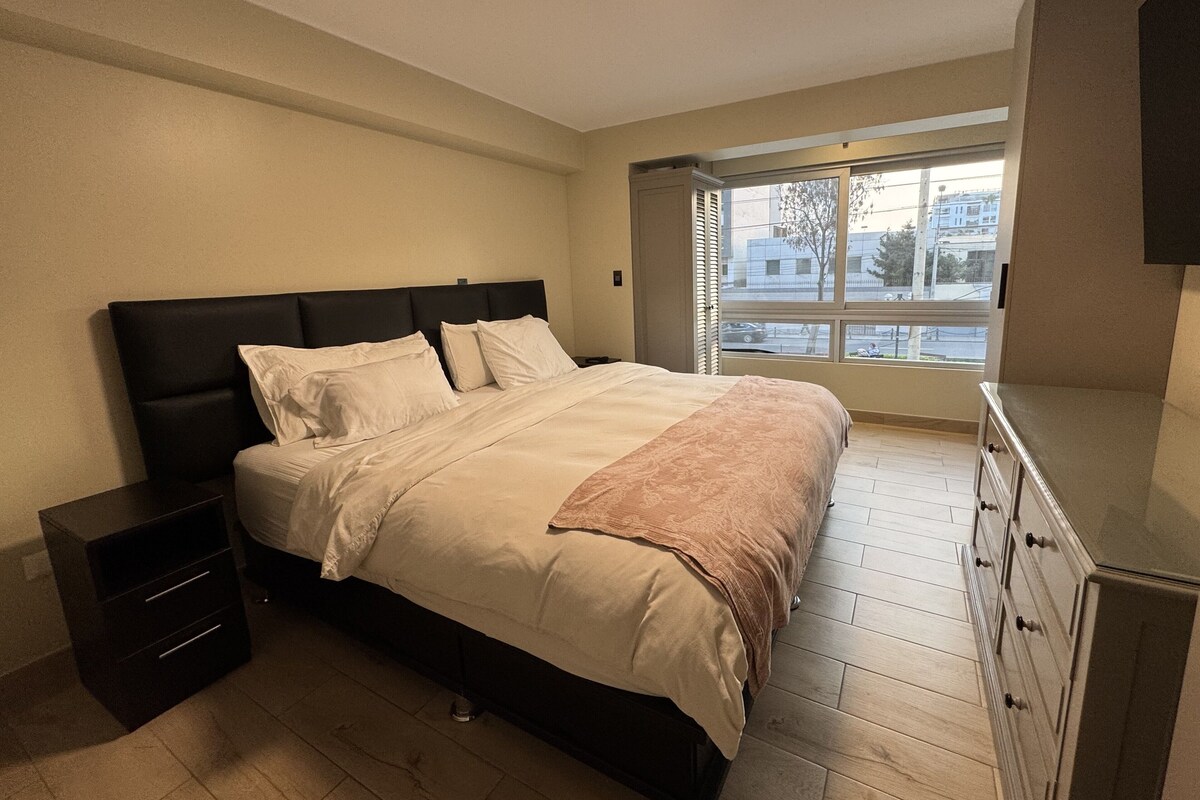 A bedroom with a bed, nightstands, a dresser, and a window with a view of the outside.