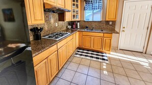 Una cocina con armarios de madera, estufa a gas, refrigerador, pileta y ventana con cortinas.