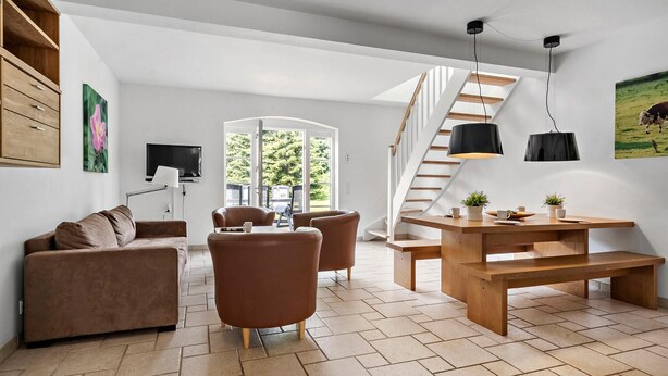 A modern living room with a sofa, chairs, a wooden table, a TV, and a staircase.