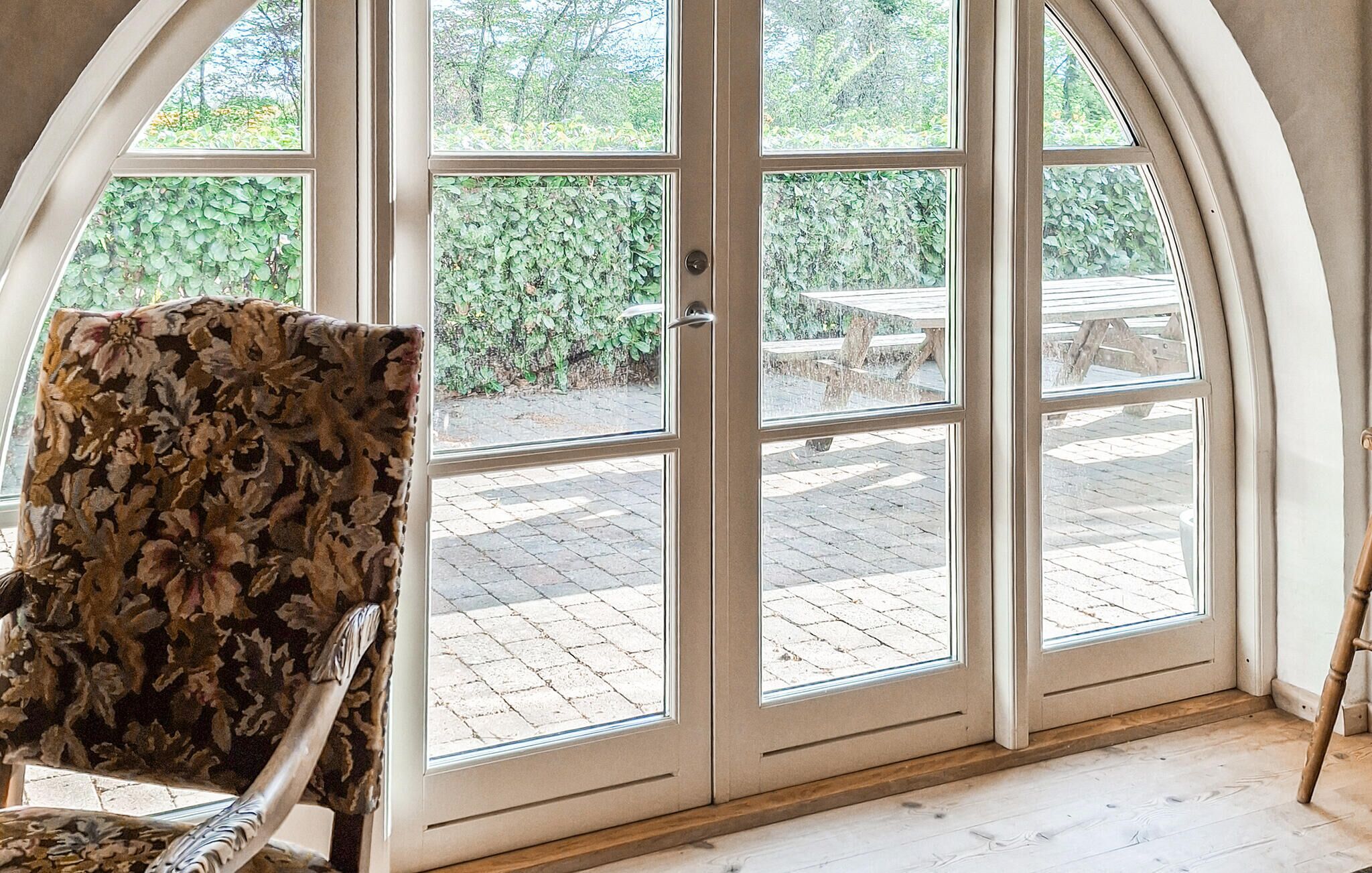 A room with a large arched glass door leading to an outdoor patio with a table and chairs.