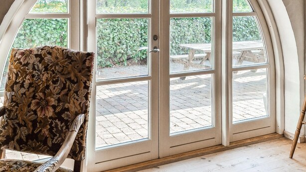 A room with a large arched glass door leading to an outdoor patio with a table and chairs. - Lovely home in Nimtofte with WiFi (Nimtofte)