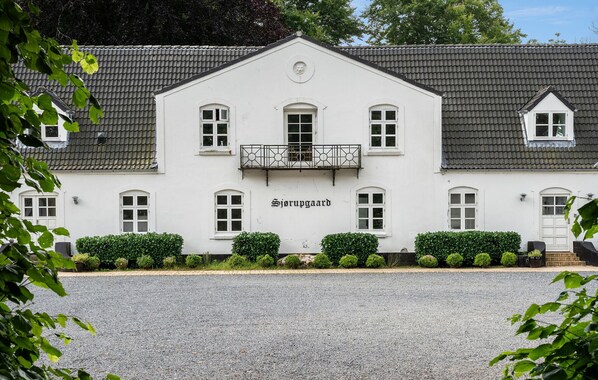 Een gebouw met een witte gevel, een balkon met een metalen hekwerk, en de naam 'Sjørupgaard' op de gevel.