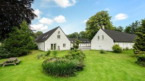 A two-story white building with a sloped roof, surrounded by a well-maintained lawn and various shrubs. - Lovely home in Nimtofte with WiFi (Nimtofte)
