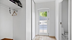 A hallway with a wooden bench, a white door leading outside, and a white toilet visible to the right.