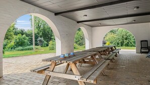 An outdoor covered picnic area with wooden benches and tables, surrounded by brick flooring and white arches. - Stunning apartment in Nimtofte with WiFi (Nimtofte)