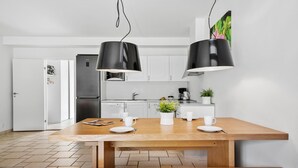 A modern kitchen with white cabinets, a stainless steel refrigerator, a wooden dining table with white plates, and two black pendant lights. - Stunning apartment in Nimtofte with WiFi (Nimtofte)