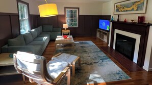 A living room with a sectional sofa, a coffee table, a TV, a fireplace, and a large window. - Family-friendly home, beautiful fenced-in yard, short walk to Ball State Campus (Muncie)