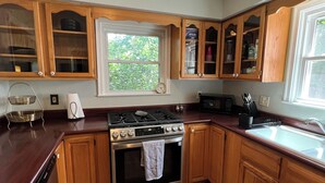 A kitchen with wooden cabinets, a stainless steel stove, and a window with a view of greenery. - Family-friendly home, beautiful fenced-in yard, short walk to Ball State Campus (Muncie)