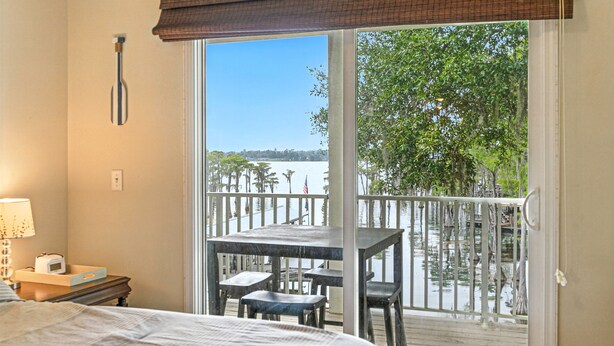 A bedroom with a large window and a balcony with a table and chairs. - Compass Lake - Cypress Sunsets! (Alford)