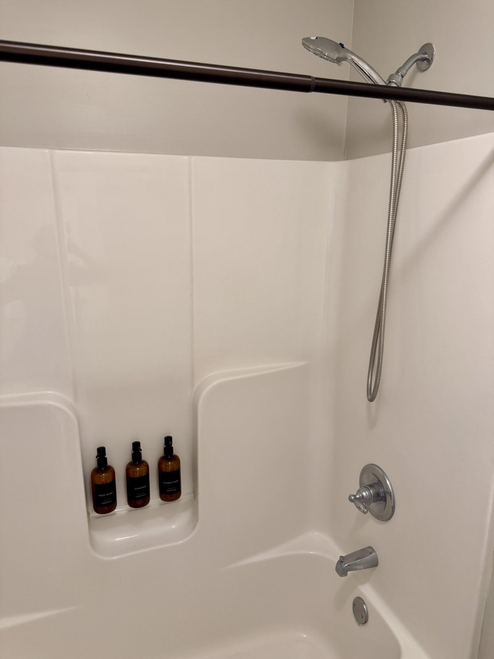 A white bathtub with a showerhead and three bottles of shampoo.