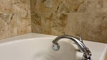 A bathroom with a white bathtub, a chrome faucet, and beige marble tiles on the walls.