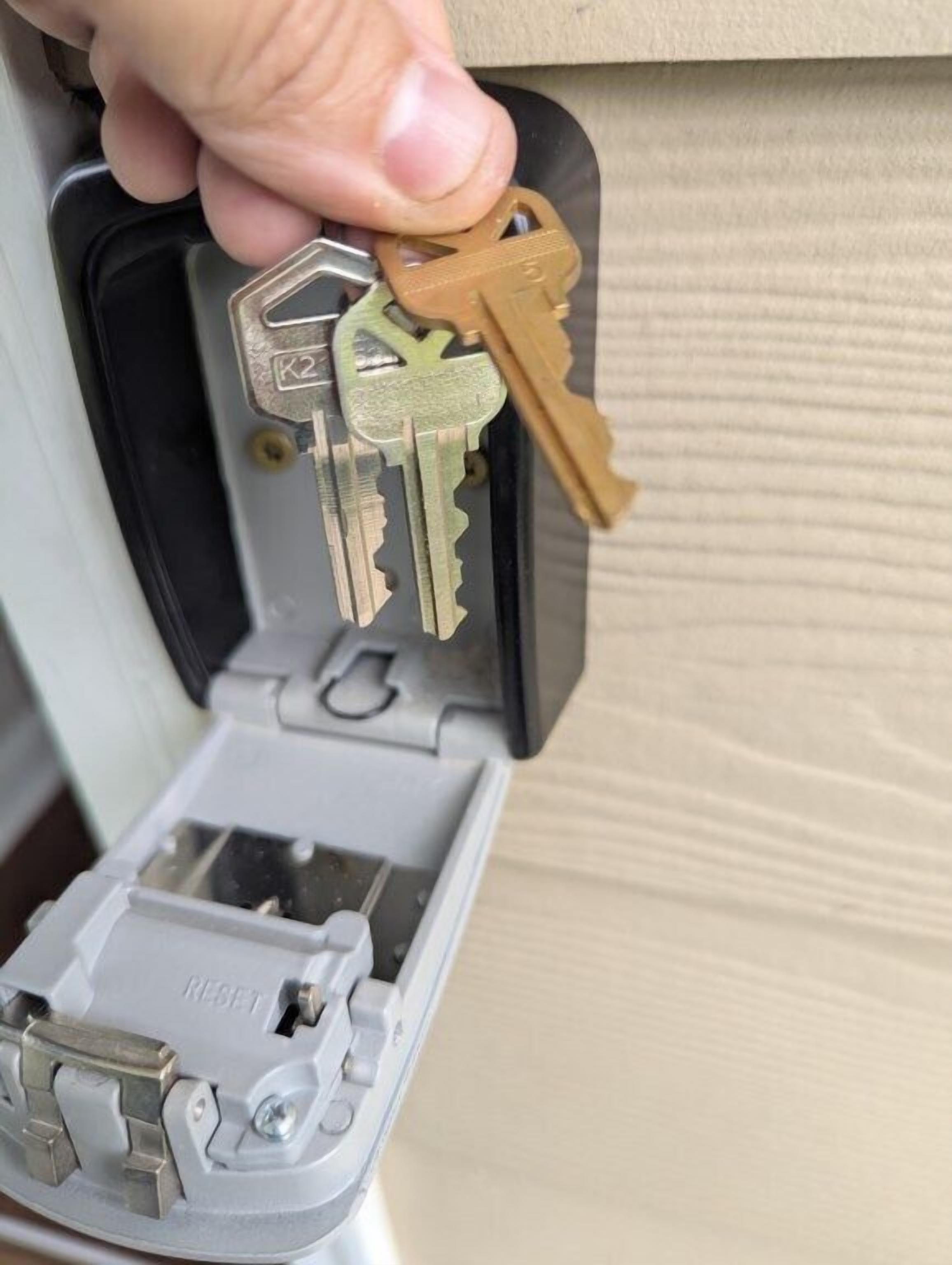 A hand holding keys above a key storage device with a reset button.