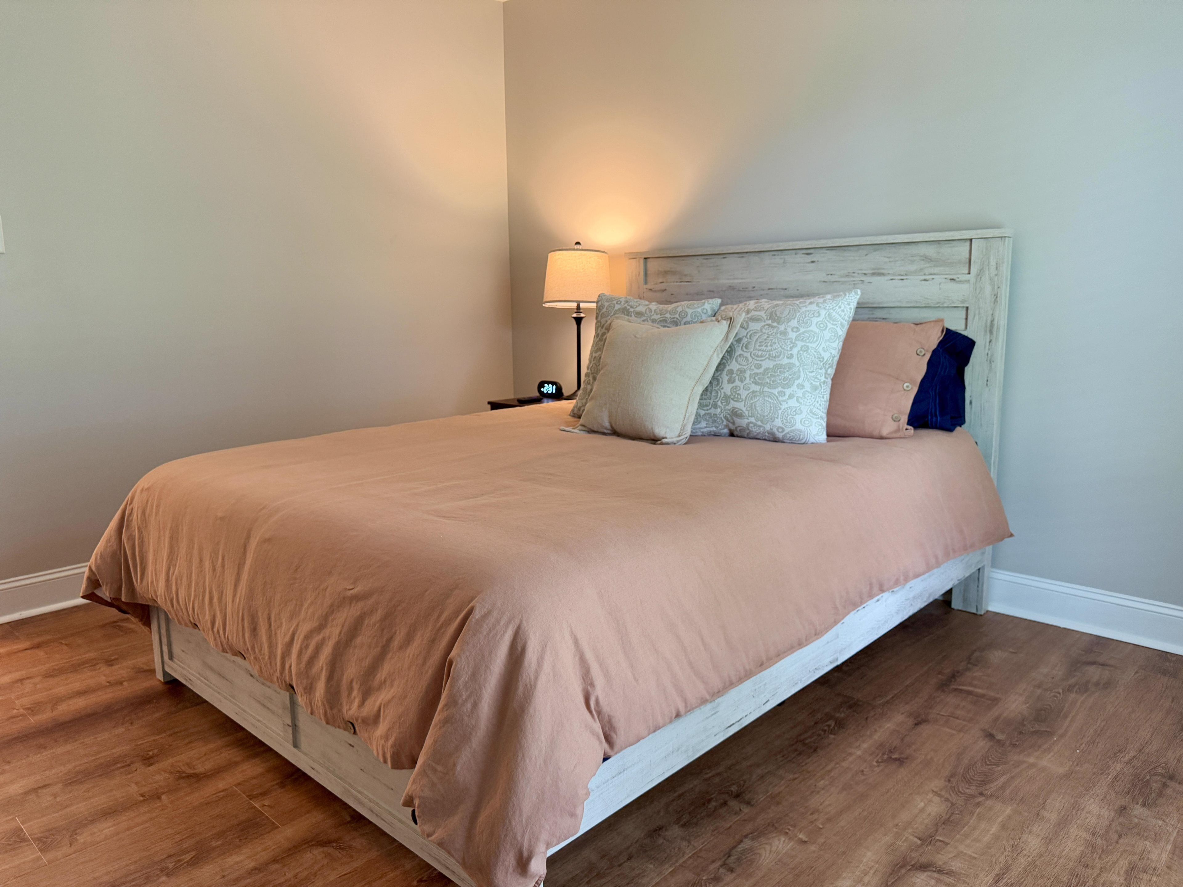 A bedroom with a bed, a nightstand, a lamp, and a wall clock.