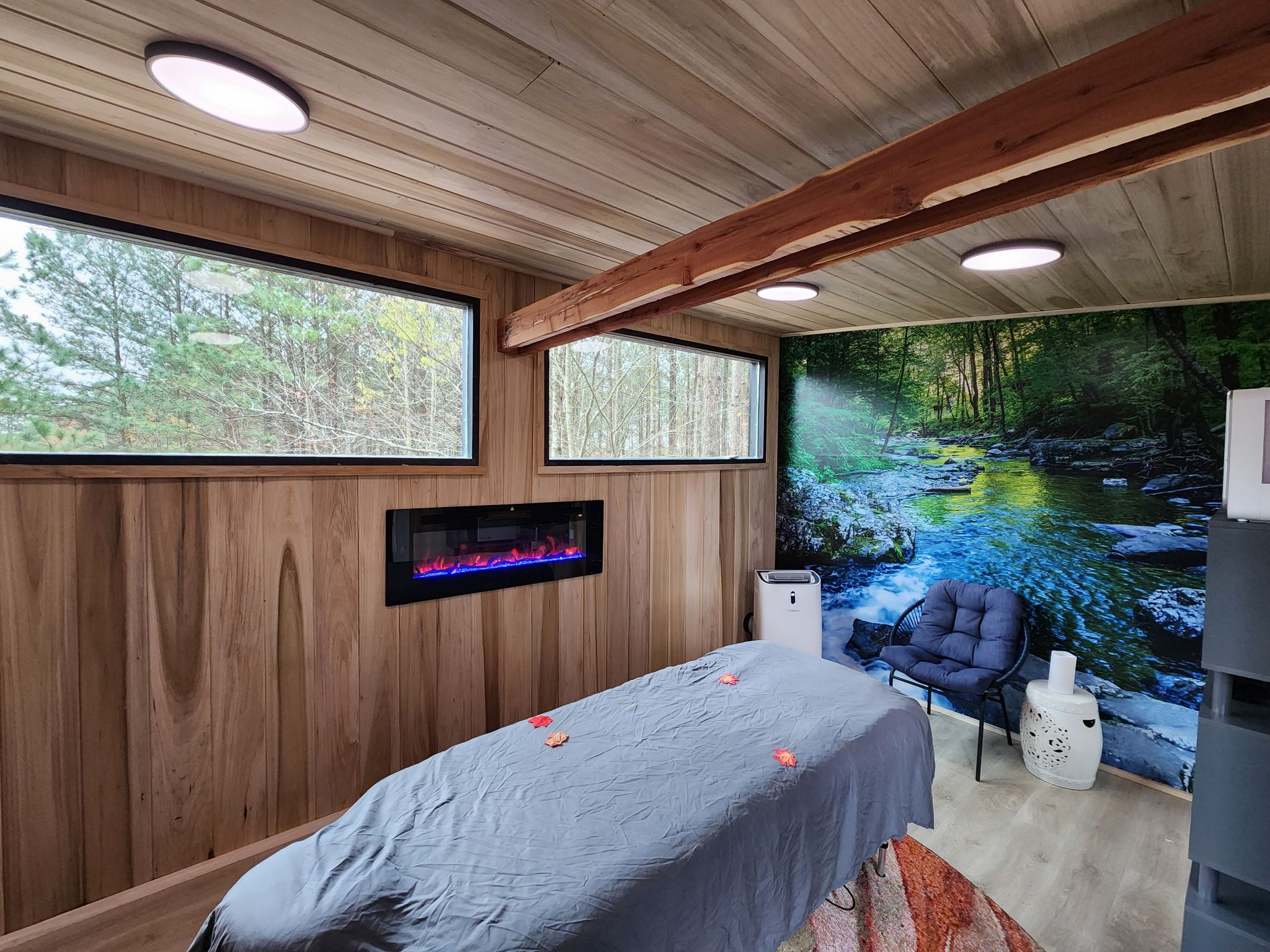 Una habitación con cama, una silla, una chimenea y un amplio ventanal con vistas al bosque.