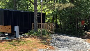 Un chemin de gravier mène à une terrasse en bois et à un bâtiment noir doté d’un escalier en bois.