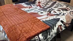 Un lit recouvert d’une couvre-lit à motifs, d’une courtepointe marron et doté d’une grande fenêtre donnant sur des arbres.