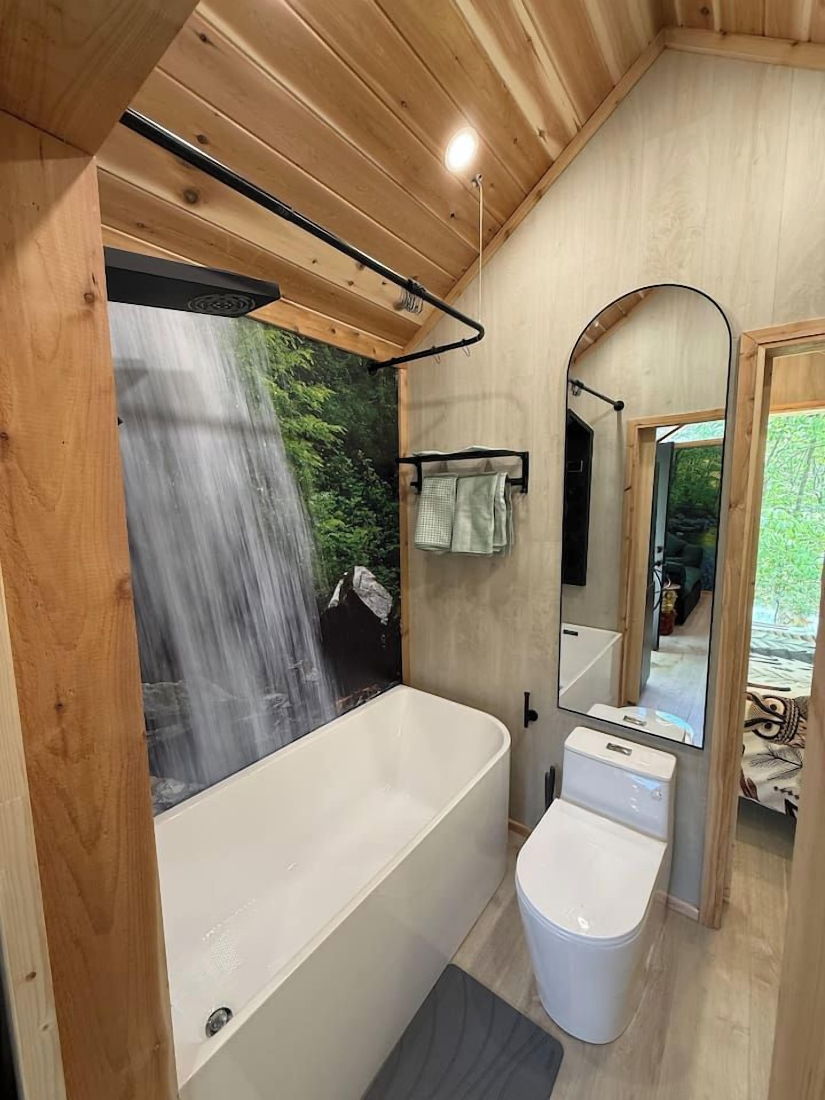 Un baño con bañera, inodoro y ducha, con vista a una cascada.