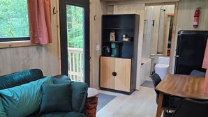 L’intérieur d’un chalet accueillant, avec un canapé vert, une table à manger en bois et un coin cuisine.