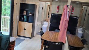 L’intérieur de ce chalet accueillant est doté de murs et d’un plafond en bois, d’un coin repas avec une table et des chaises, d’un coin cuisine avec un réfrigérateur et d’un petit coin salon avec un canapé et des coussins.