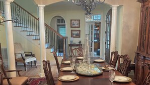 A formal dining room with a large wooden table set for six, surrounded by ornate chairs. A chandelier hangs above the table, and the room features a staircase with a railing and a view into another room with bookshelves. - Spacious 4 Bed 3 Bath Auburn Game Day Home (Auburn)