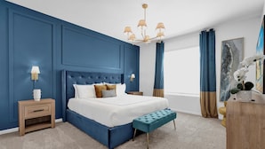 Une chambre à coucher avec un grand lit, une table de chevet, un banc, un lustre et une fenêtre avec des rideaux.