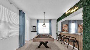 Une table de billard dans une pièce moderne, avec un coin bar et un mur vert.
