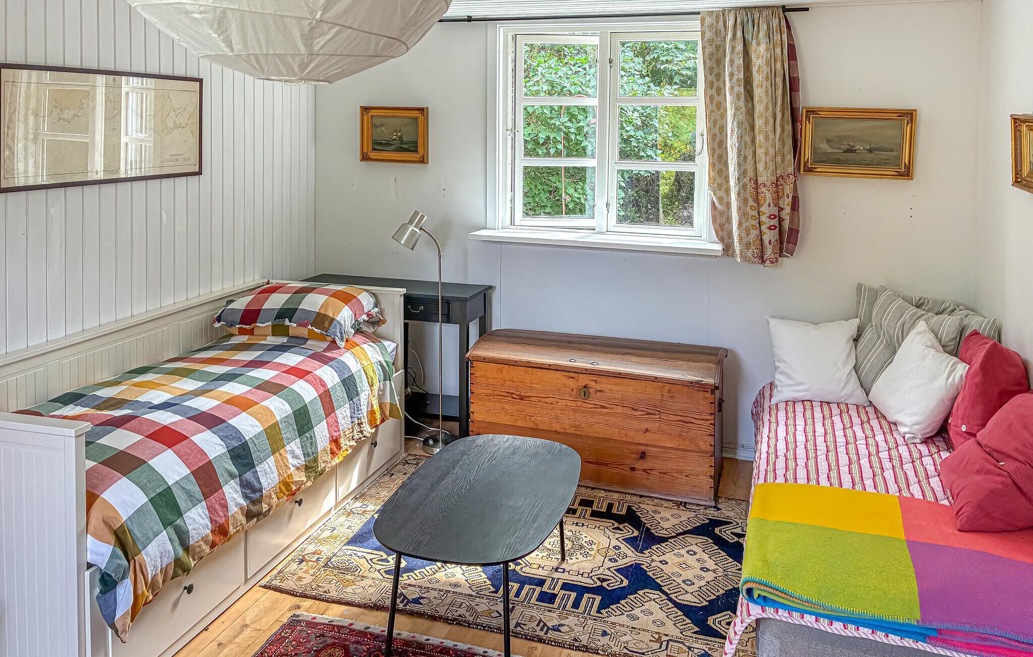 A cozy bedroom with a bed, a chest of drawers, a desk, and a window with curtains.