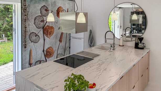 A modern kitchen with a marble countertop, a sink, a stove, and a mirror. There is a plant and a bowl of fruit on the counter. - 4 bedroom nice home in Gilleleje (Gilleleje)