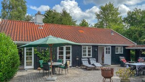 A house with a tiled roof, a covered patio with a table and chairs, and a lounge area with sun loungers. - 4 bedroom nice home in Gilleleje (Gilleleje)