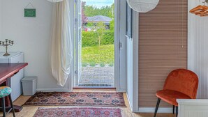A room with a sliding glass door leading to a garden, a wooden table, a red chair, and a patterned rug. - 4 bedroom nice home in Gilleleje (Gilleleje)