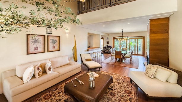 A spacious living room with a high ceiling, a dining area, and a balcony with a view of the outdoors.