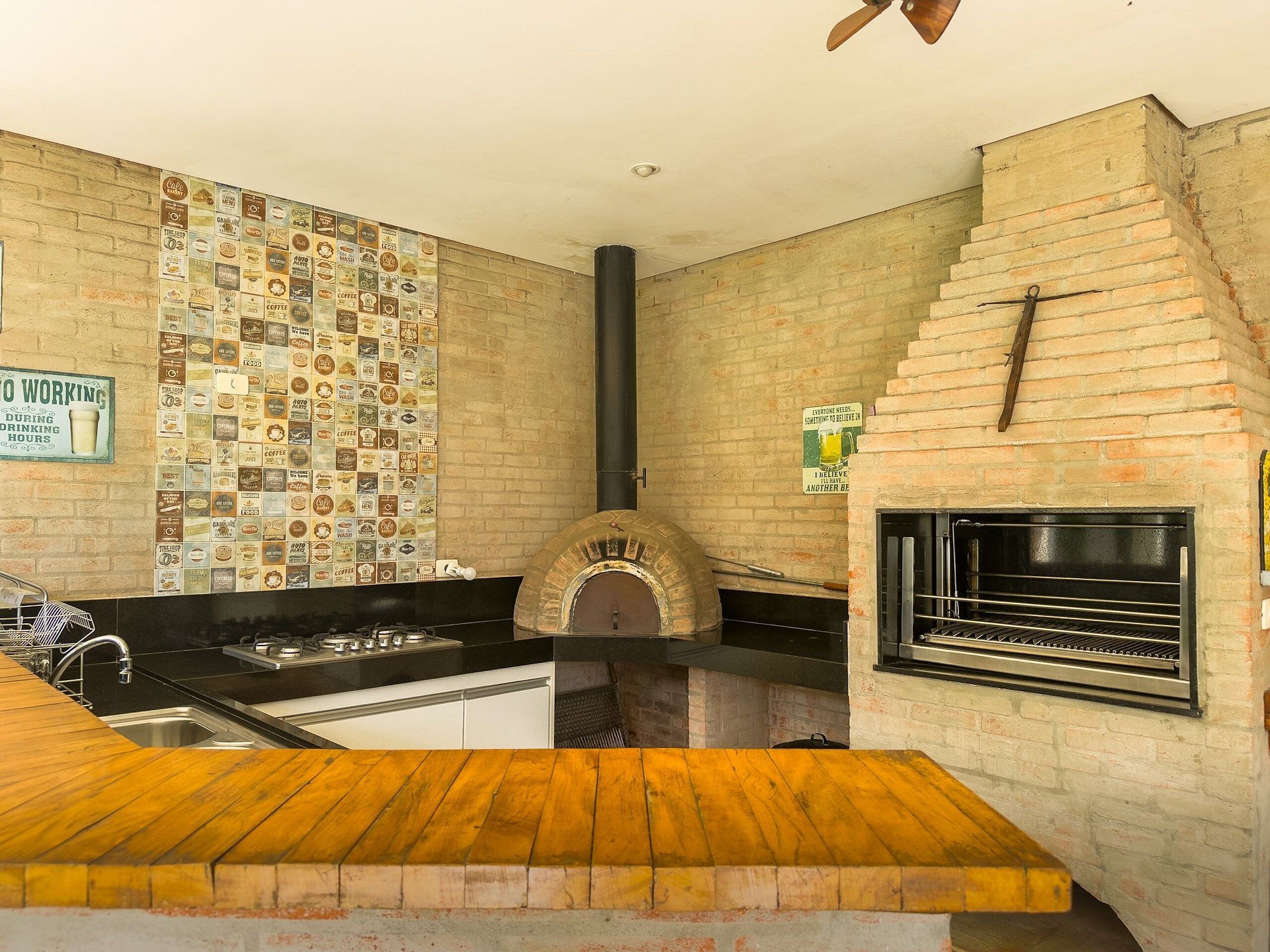 A kitchen with a brick wall, a coffee-themed wall art, a pizza oven, and a grill.