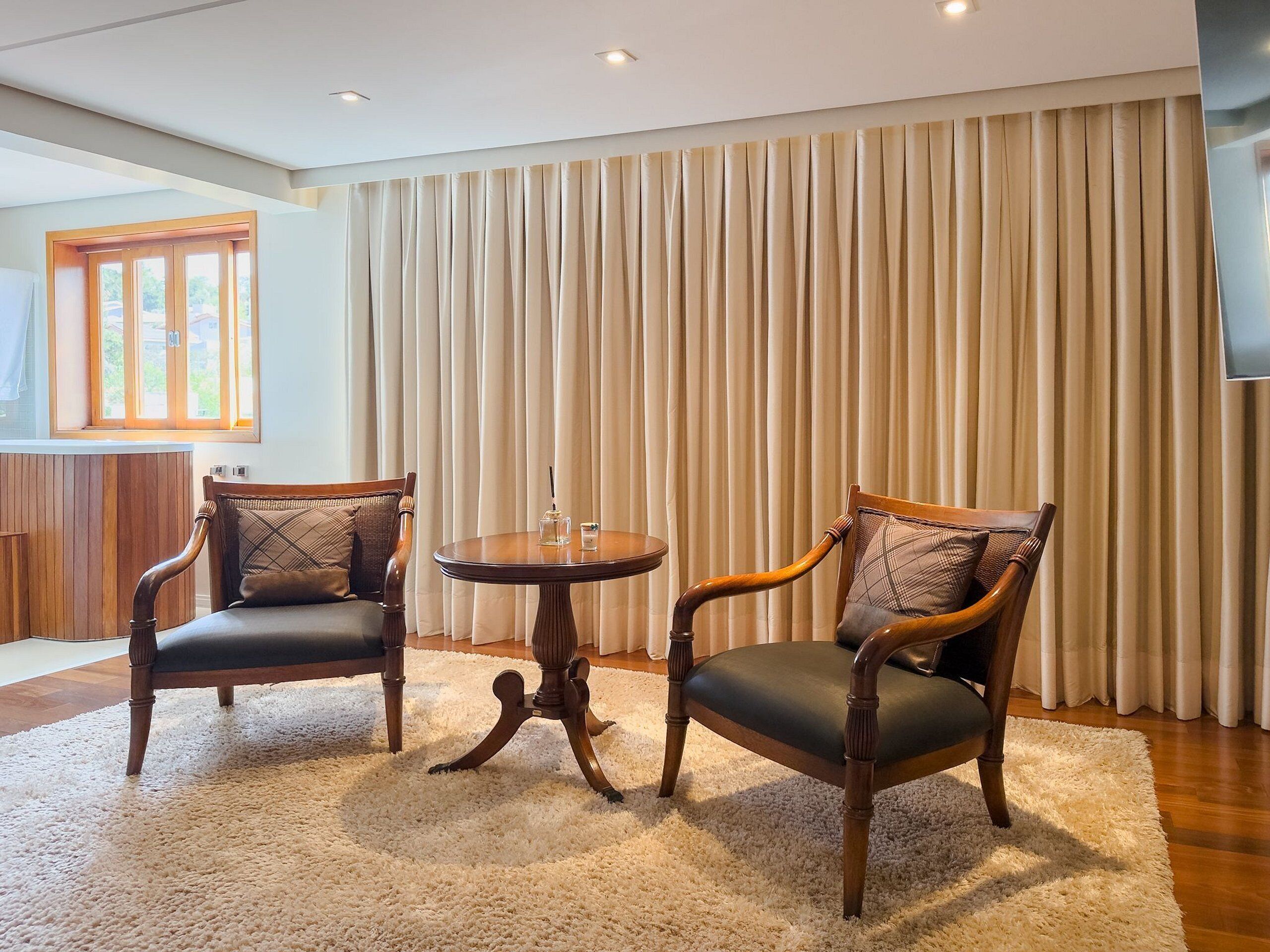A room with two wooden armchairs, a small round table, and a large window with curtains.