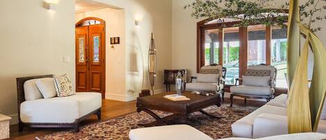 A spacious living room with a large window, a sofa set, a coffee table, and a decorative plant.