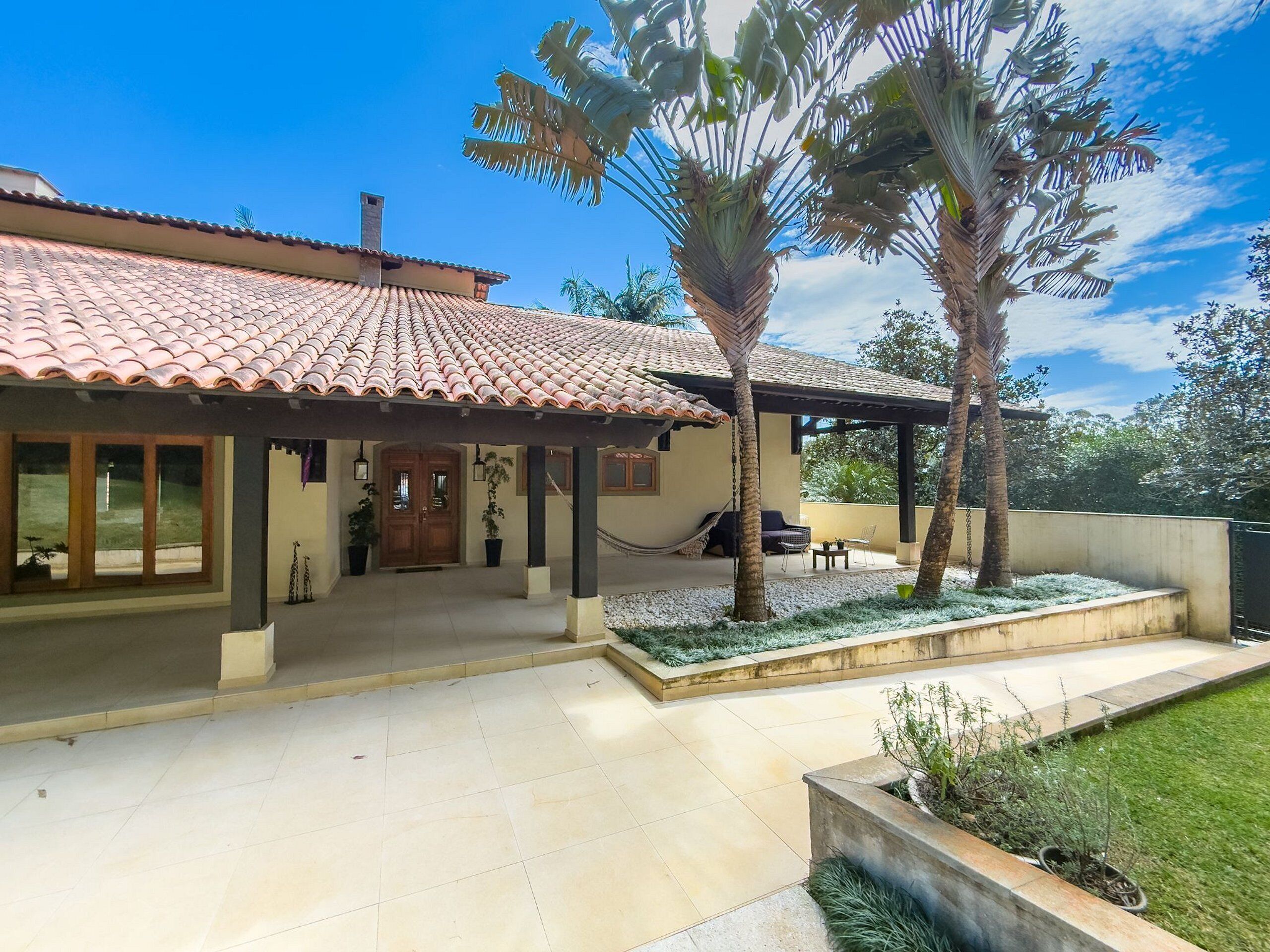 Una casa con techo de tejas, un porche cubierto y un jardín con palmeras.