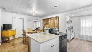 A modern kitchen with white cabinetry, a wooden dining table, and a black stove. - Farmhouse on Main - historic home in the heart of Riggins (Riggins)