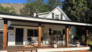 A house with a covered porch, a dining area with chairs and a table, and a garage door with the number 509. - Farmhouse on Main - historic home in the heart of Riggins (Riggins)