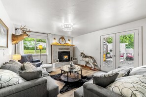 A living room with a fireplace, grey sofas, a round coffee table, and a mounted deer head. - Farmhouse on Main - historic home in the heart of Riggins (Riggins)
