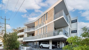 A modern multi-story residential building with a covered parking area and a white car parked inside. - Scarborough Pearl Apartment (Scarborough)