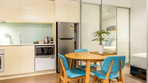 A compact kitchen with a microwave, refrigerator, and a small oven. There is a round wooden table with blue chairs and a potted plant. - Scarborough Pearl Apartment (Scarborough)