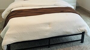 Een net opgemaakt bed met een witte dekbedovertrek en een bruine plaid, aan weerszijden voorzien van wandlampen met gouden details.