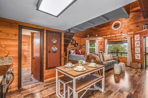 A wooden cabin interior with a dining table, sofa, and a staircase leading to a loft. - Lookout Point - Firepit, Pickle Ball, Balcony, Pet (Sevierville)