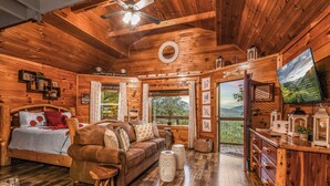 A wooden cabin interior with a bed, sofa, dining table, and a TV. - Lookout Point - Firepit, Pickle Ball, Balcony, Pet (Sevierville)